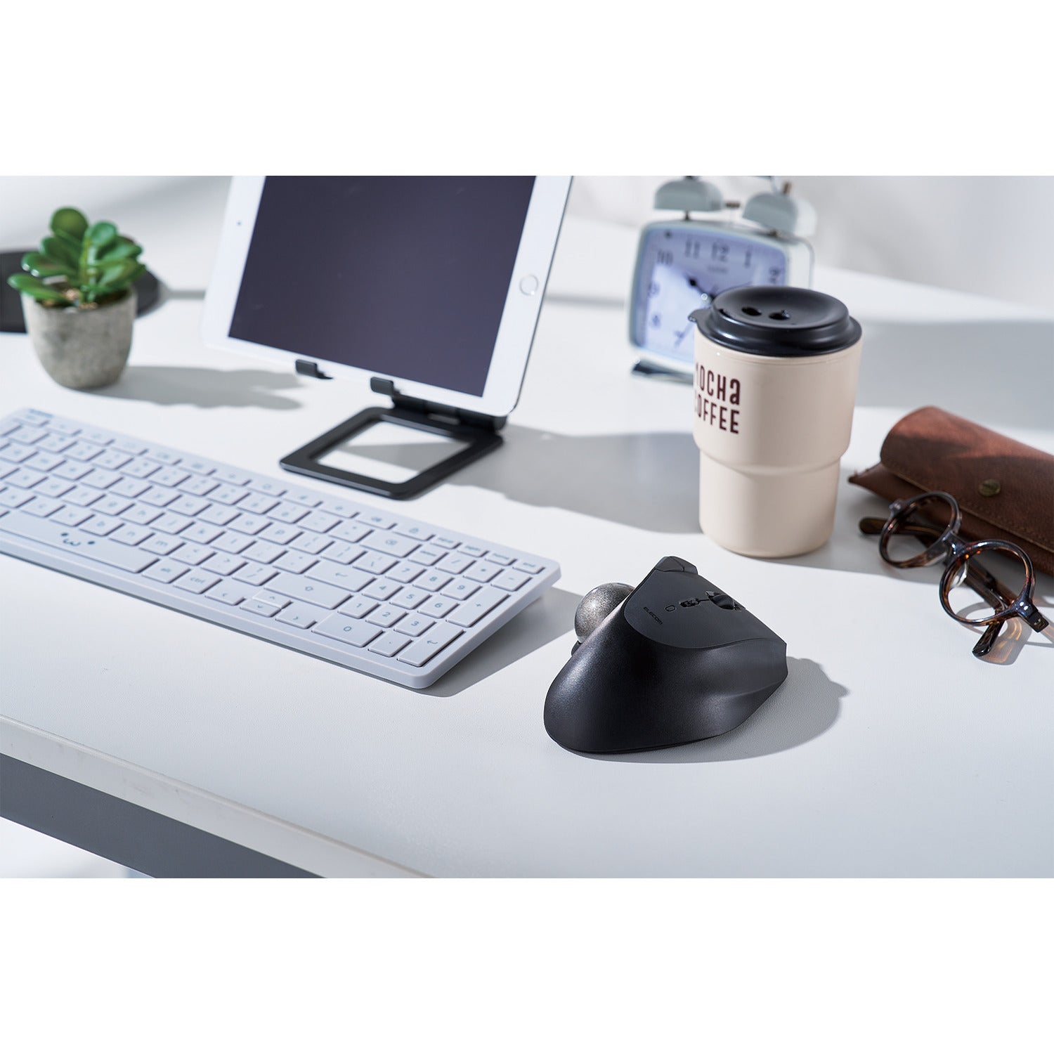black and silver RollMaster bluetooth trackball mouse | similar to microsoft explorer trackball mouse | lifestyle image with shiro chan keyboard, ipad on ipad stand, coffee cup, and glasses on white desk