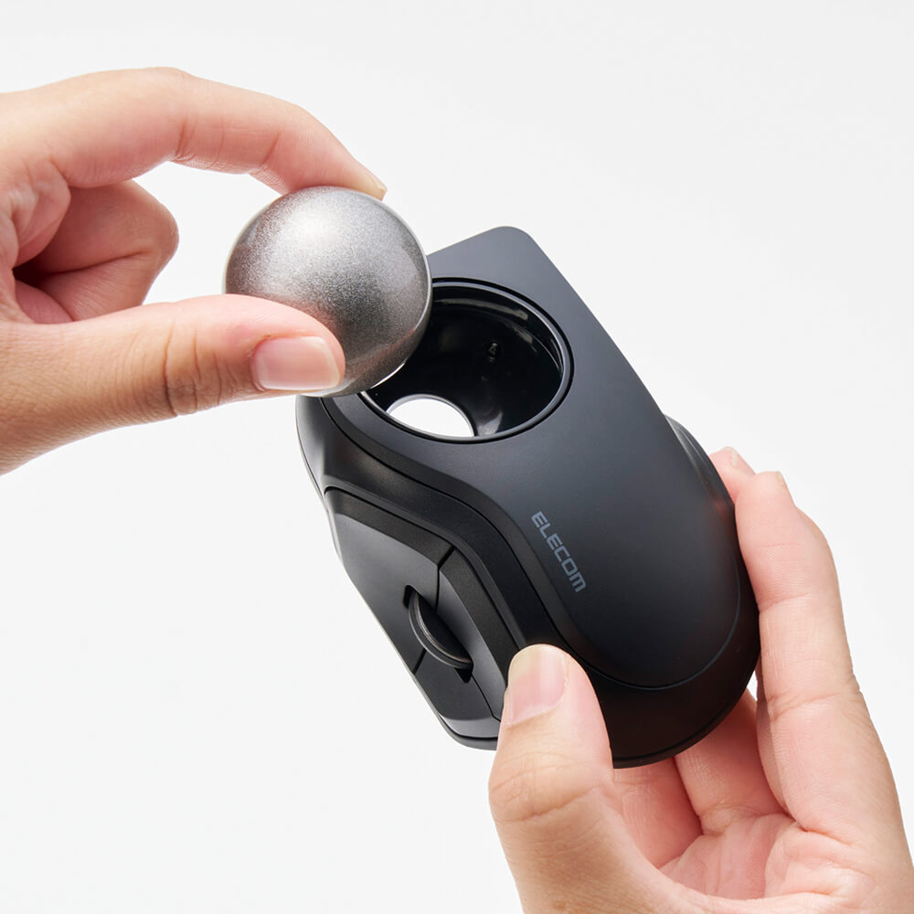 A person holds a black bitra index trackball mouse with a metallic silver ball inside its opening, shown against a clean white background.