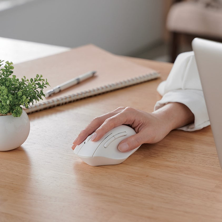 White SH20 Ergonomic Mouse Bluetooth hand using white mouse next to a laptop spiral notebook pen on wooden desk | Elecom Ergonomic Bluetooth Mouse