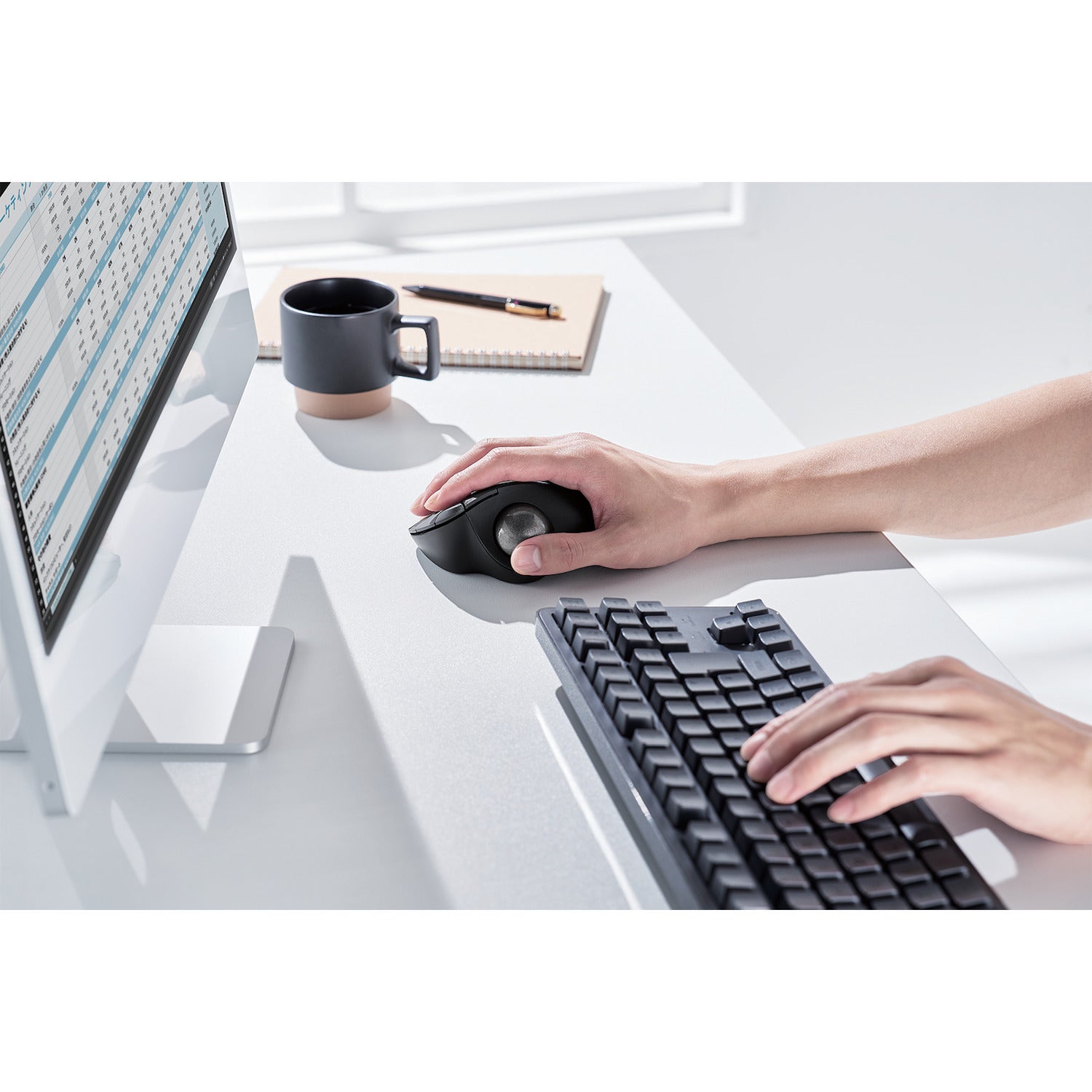 side top view of person using black ergonomic trackball mouse with silver ball | trackball mouse with programmable buttons | lifestyle image with black coffee cup and black keyboard on white desk with white computer monitor