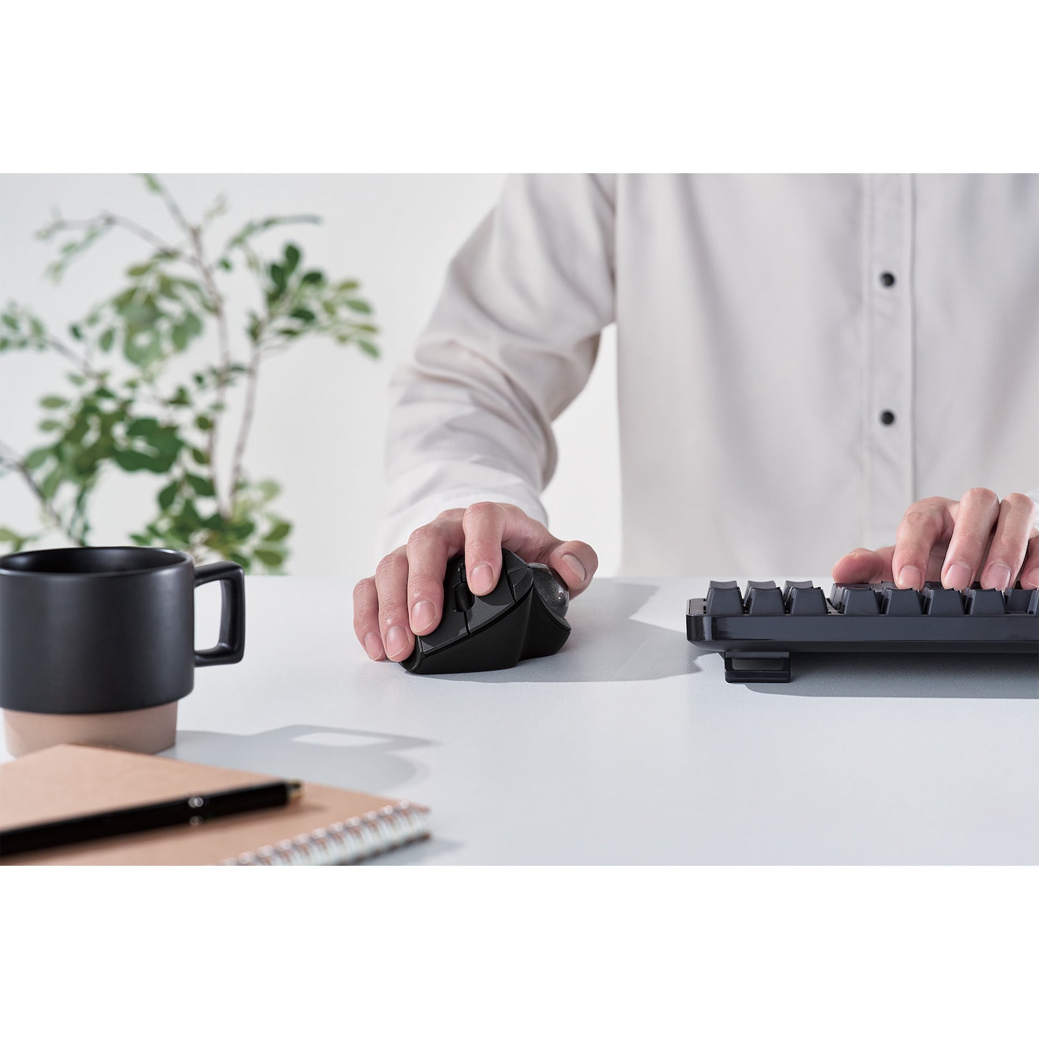 front view black ergonomic trackball mouse with silver ball | trackball mouse with programmable buttons | lifestyle image with black coffee cup and black keyboard on white desk