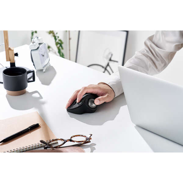 lifestyle image of thumb controlled black trackball mouse with silver oversized ball | white desk with silver laptop, glasses, and black coffee cup